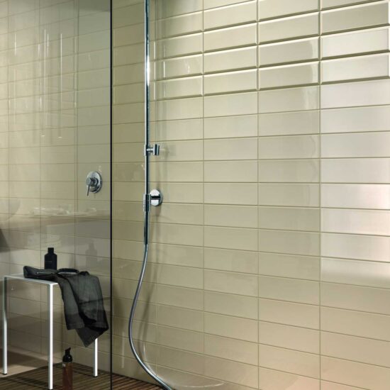 Doccia moderna con soffione cromato, parete in piastrelle chiare e un tappetino in legno. Elementi di design essenziali.